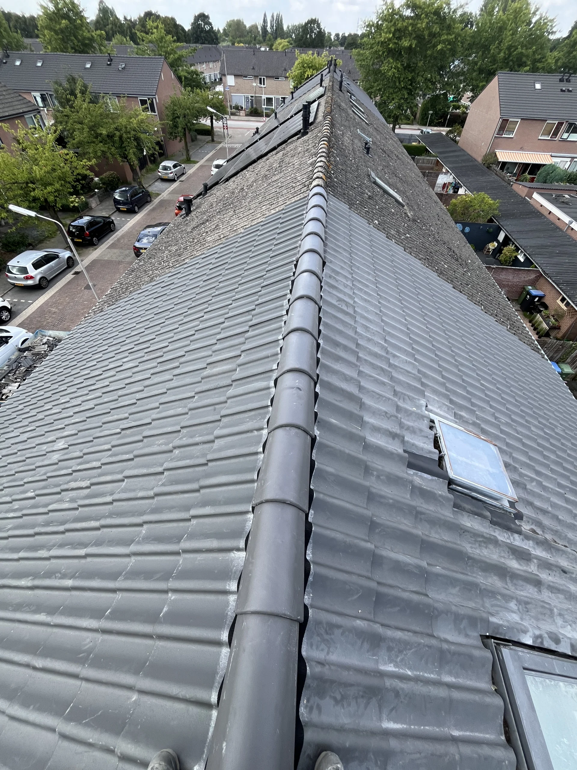 Overzicht van een vakkundig hersteld pannendak met nieuwe grijze nokvorsten in Den Haag.