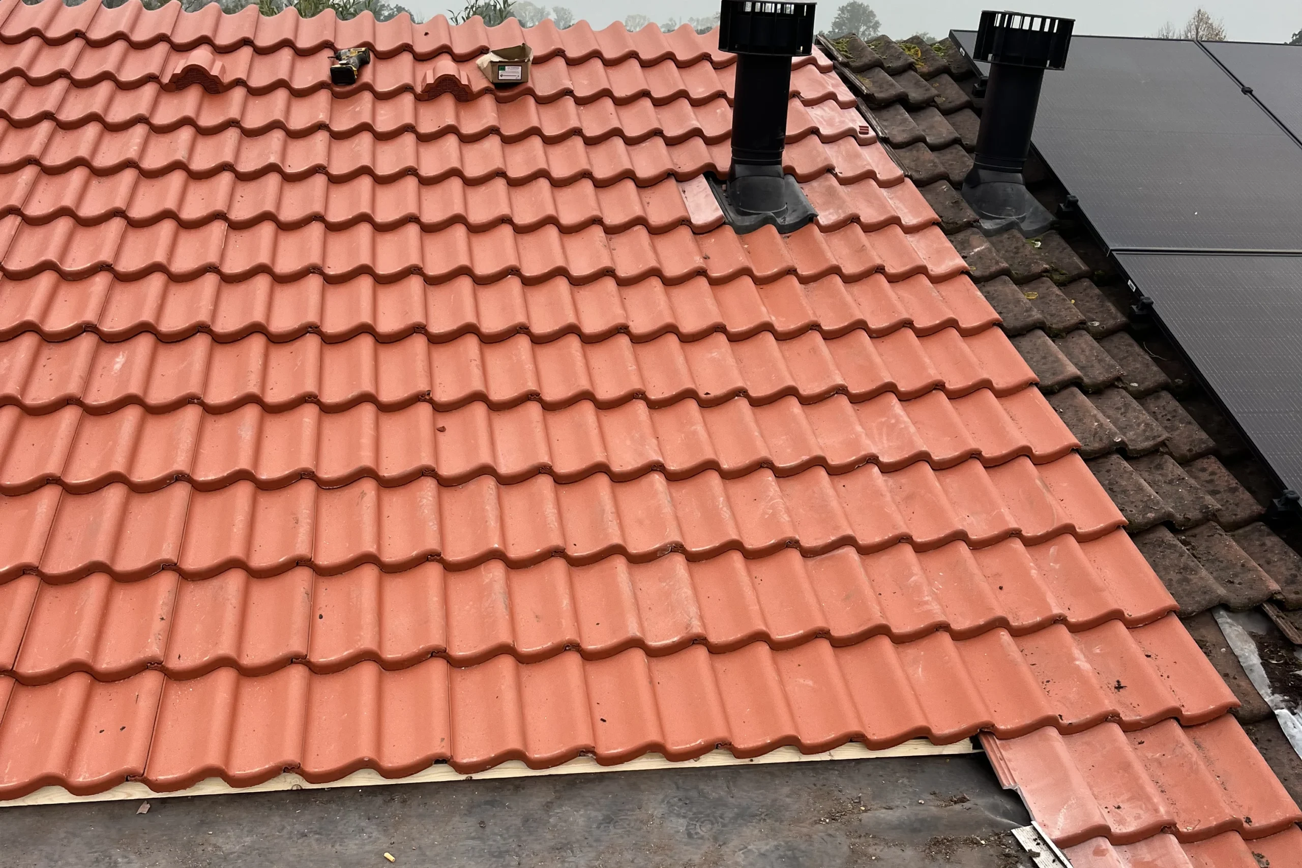 Vakkundige dakrenovatie in Den Haag door De Dakdekker Den Haag waarbij nieuwe rode dakpannen en ventilatiedoorvoeren op een hellend dak worden geplaatst.