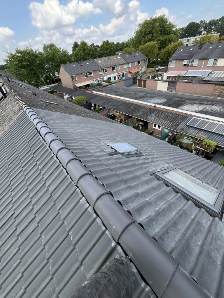 Vakkundige renovatie van een hellend dak met grijze dakpannen en een dakraam in Den Haag door De Dakdekker Den Haag.