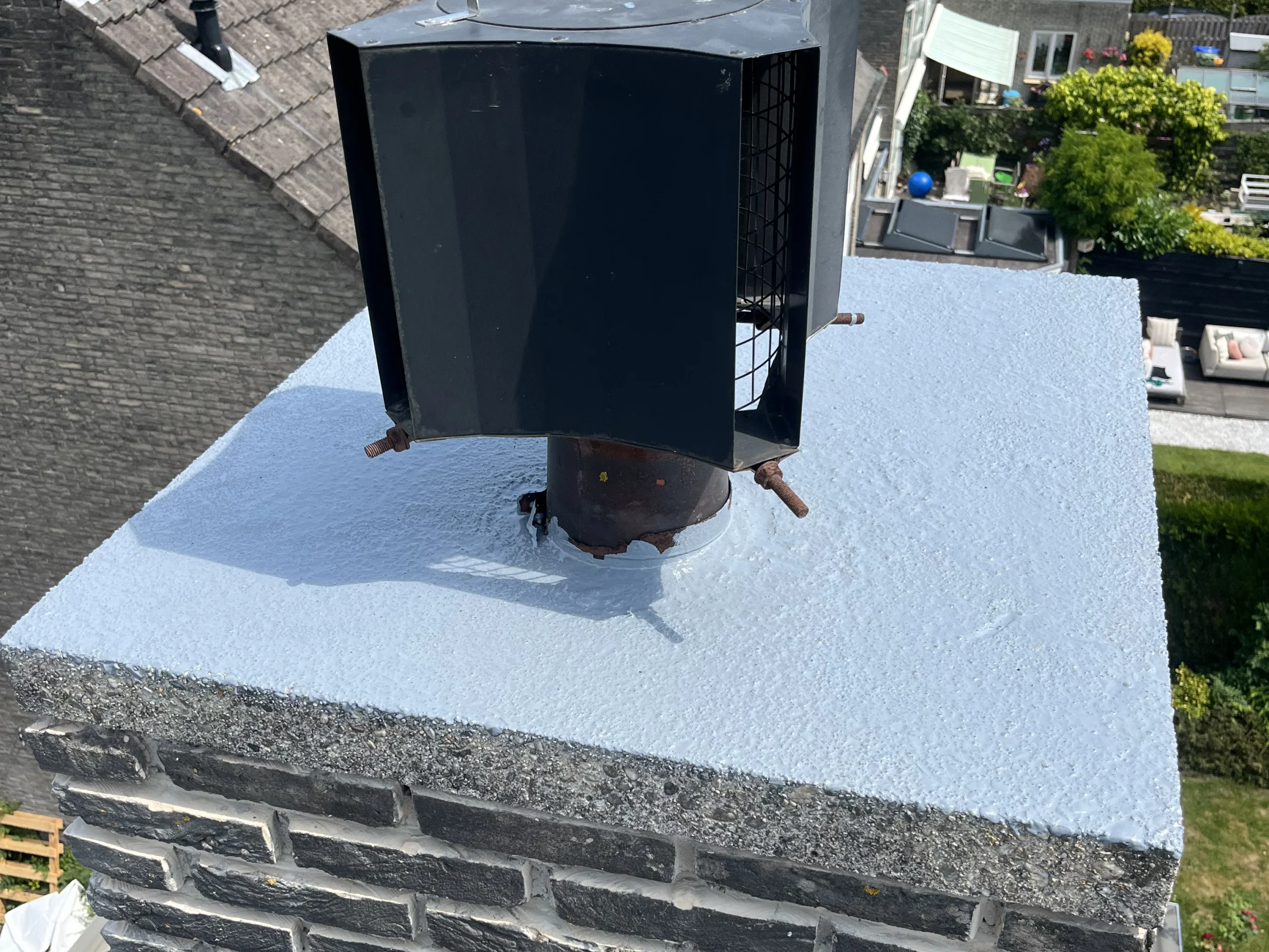 Detailopname van een schoorsteenrenovatie in Den Haag met een nieuwe waterdichte coating op de bovenplaat en een gemonteerde schoorsteenkap.