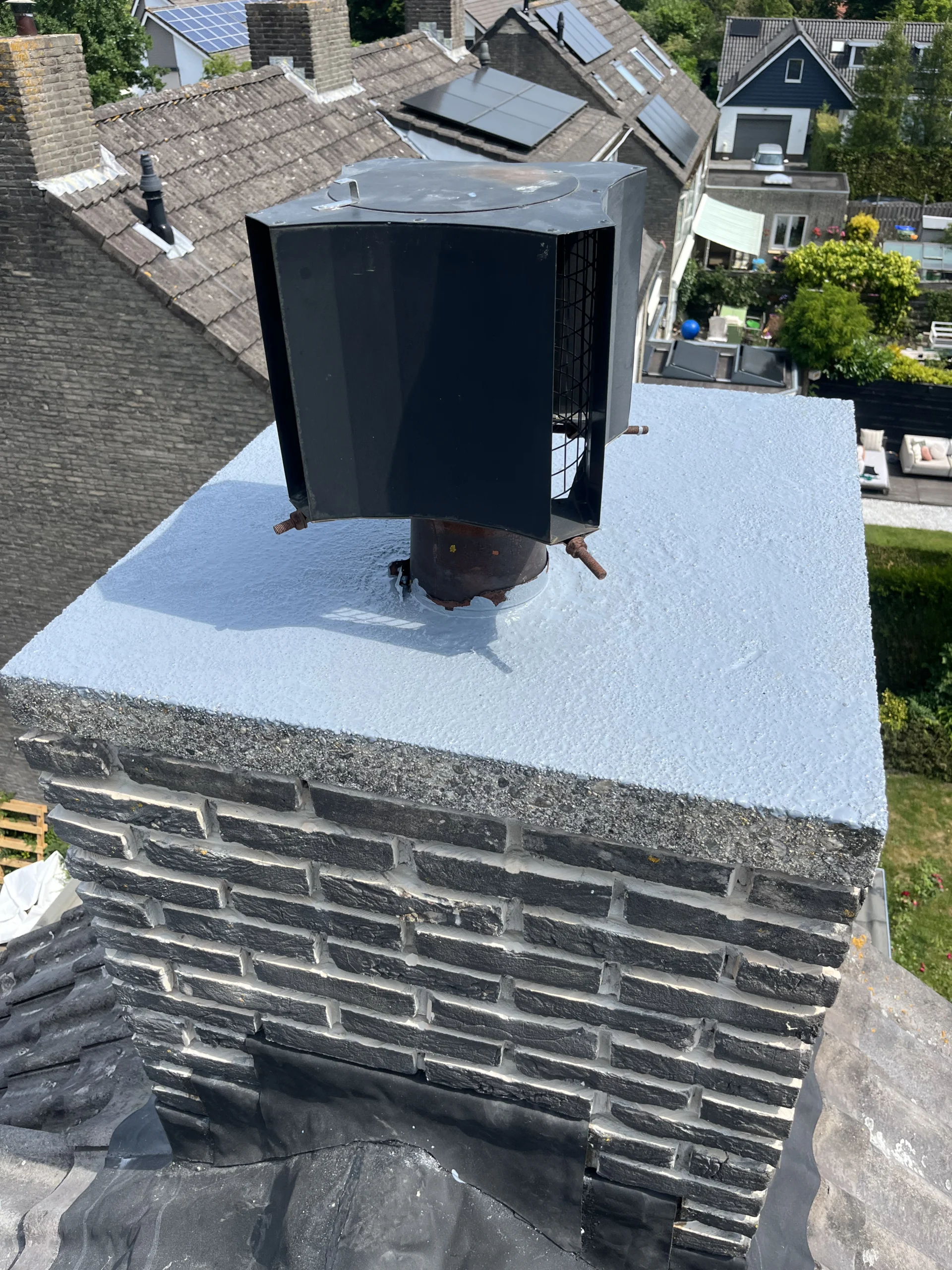 Detailopname van een schoorsteenrenovatie in Den Haag met een nieuwe waterdichte coating op de bovenplaat en een gemonteerde schoorsteenkap.